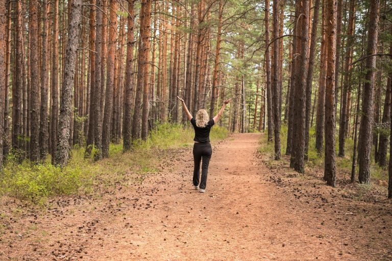 Žena se rozpaženýma rukama na lesní cestě — pohyb v přírodě a zdraví mozku