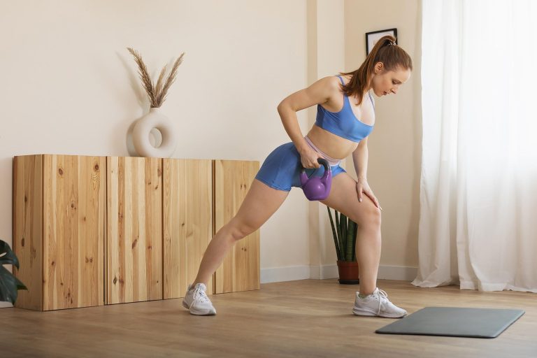 Žena cvičí kettlebell doma — výpad s kettlebellem, trénink pro začátečníky